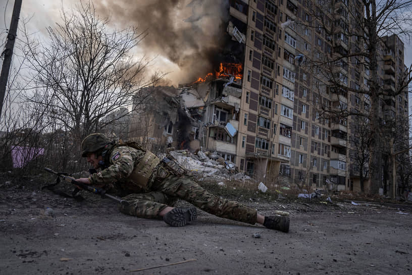Украинский полицейский укрывается перед горящим зданием в Авдеевке