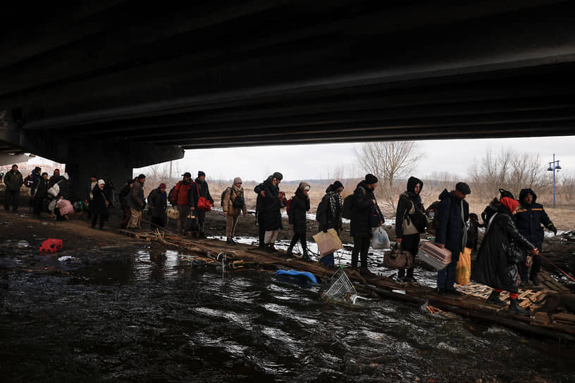 Люди с вещами под разрушенным мостом переходят реку Ирпень