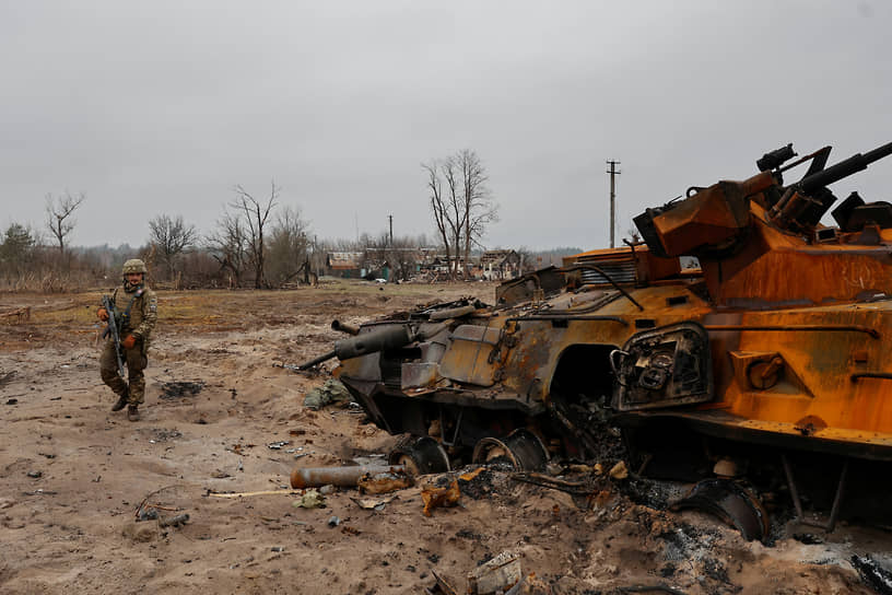 Военнослужащий осматривает сгоревший бронетранспортер в Киевской области