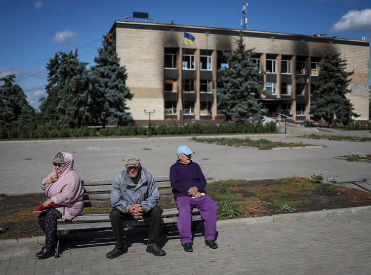 Местные жители сидят на скамейке около сгоревшего здания Изюмского горсовета