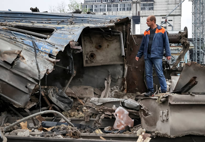 Рабочий стоит рядом с разрушенными вагонами в Харькове