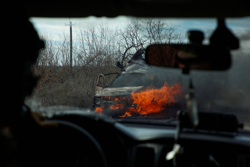 Украинские военнослужащие проезжают мимо горящего автомобиля, атакованного дроном