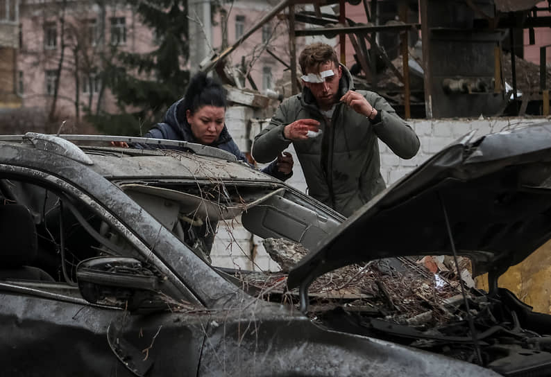 Раненый местный житель стоит возле своей поврежденной в результате ракетного удара машины в Харькове