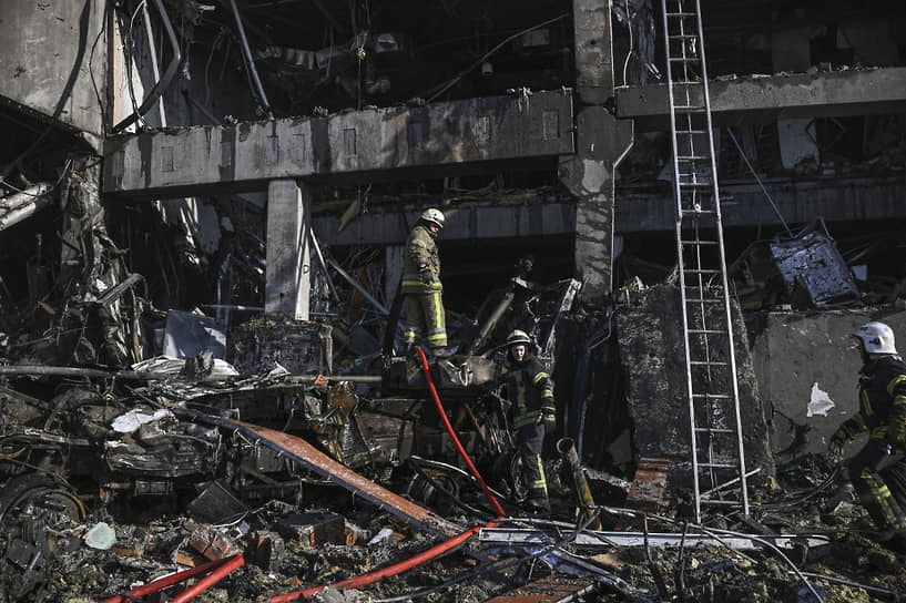 Пожарные стоят на сгоревшей бронетехнике после удара по торговому центру в Киеве