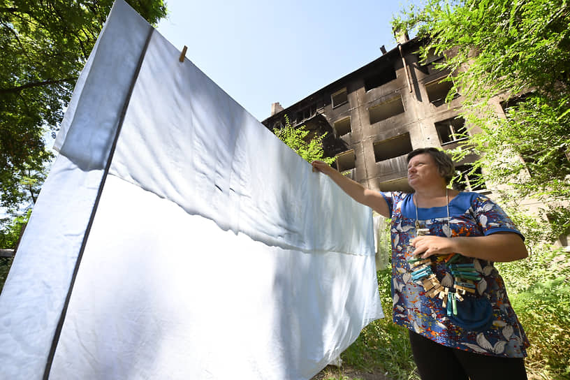 Женщина развешивает белье во дворе разрушенного многоквартирного дома