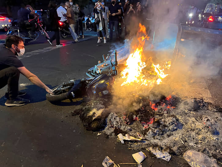 Мужчина вытаскивает из огня полицейский мотоцикл, который подожгли протестующие
