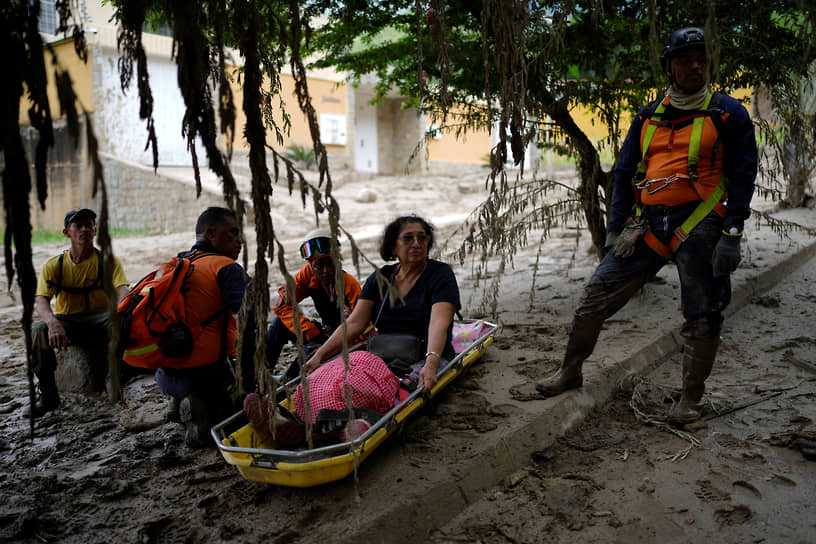 Пострадавшая в результате наводнения женщина сидит на носилках рядом со спасателями