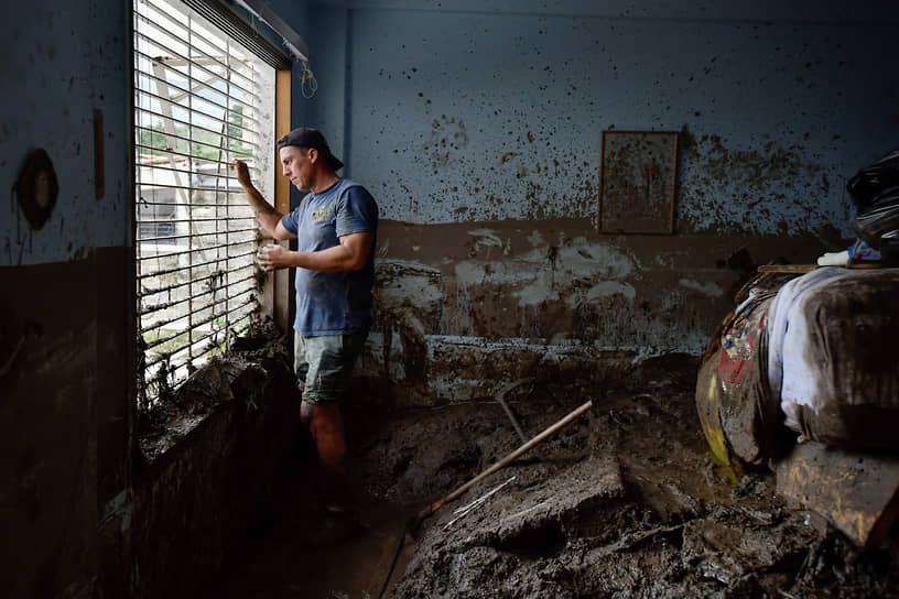 Местный житель смотрит из окна своего дома, пострадавшего от оползня 