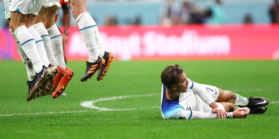 Английский полузащитник Джек Грилиш лежит на поле, пока футболист сборной Сенегала бьет штрафной