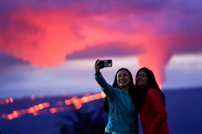 Туристки фотографируются на фоне извергающегося вулкана