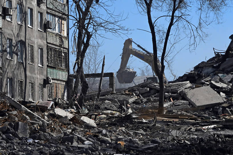 Экскаватор разбирает завалы возле разрушенного дома в Мариуполе