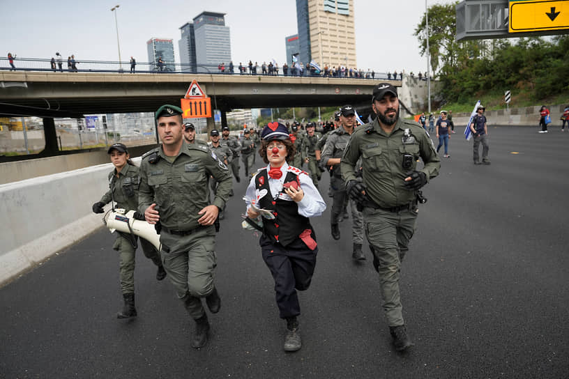 Израильский активист в костюме клоуна бежит с полицией во время протестов в Тель-Авиве