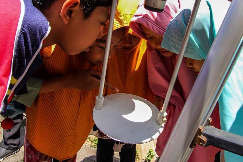 Подростки смотрят на отражение солнечного затмения на телескопе в Джокьякарте в Индонезии