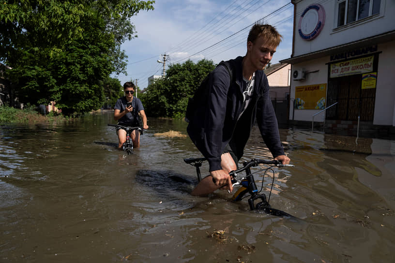 Местные жители пытаются проехать на велосипедах по затопленной дороге 