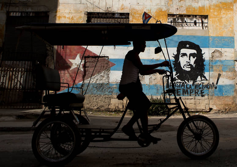 Велотакси в Гаване проезжает мимо здания с портретом Че Гевары и лозунгом «Hasta la victoria siempre» 