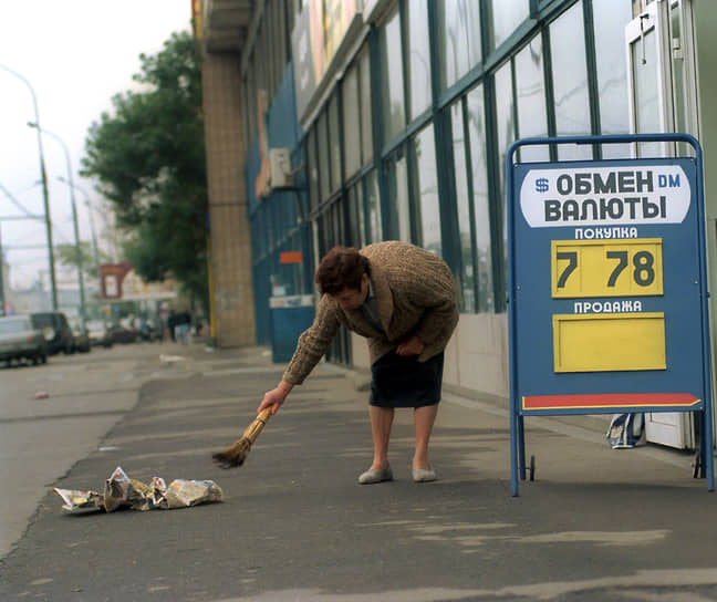 Женщина подметает тротуар возле пункта обмена валюты 