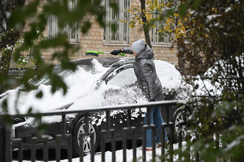 Жительница Москвы убирает снег с машины