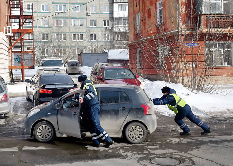 Сотрудники ДПС толкают автомобиль при выезде из двора жилого дома в Омске