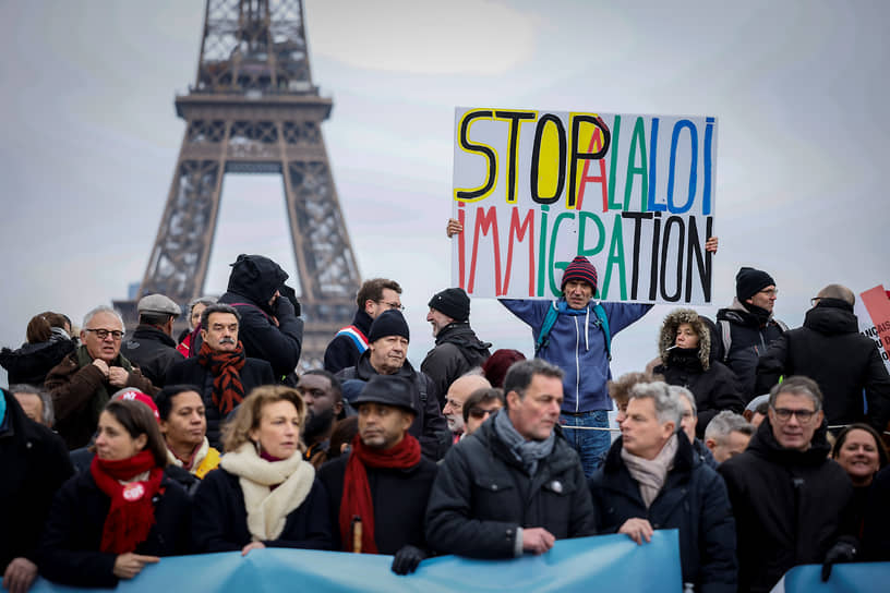 Мужчина на площади рядом с Эйфелевой башней держит плакат с надписью «Стоп иммиграционному закону» 