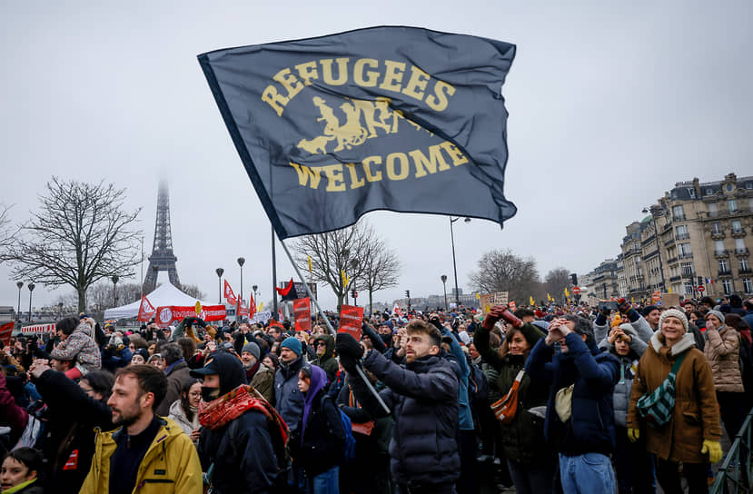 Противник иммиграционного закона держит флаг с надписью «Добро пожаловать беженцам»  
