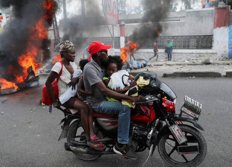 Как отмечают СМИ, в других крупных городах Гаити также есть жертвы среди участников протестов, слышны автоматные очереди
&lt;br>На фото: семья проезжает возле горящих баррикад