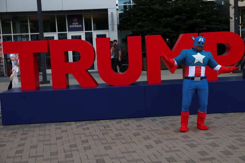 Участник Республиканского национального съезда в костюме героя комиксов «Капитана Америки» позирует на фоне инсталляции с именем Трампа