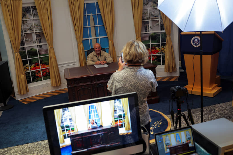 Мужчина позирует для фотографии в декорациях Овального кабинета из резиденции президента США