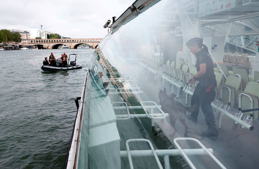Сотрудница полиции и служебная собака осматривают лодку на Сене, которая примет участие в церемонии открытия