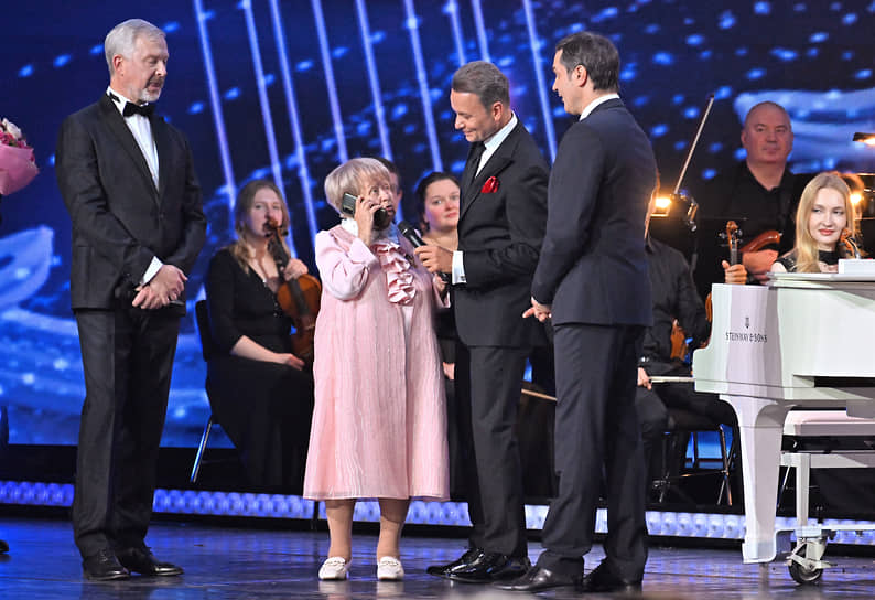 Президент РФ Владимир Путин по телефону поздравляет Александру Пахмутову с днем рождения во время концерта&lt;br>
Слева направо: телеведущий Валдис Пельш, Александра Пахмутова и актер Александр Олешко