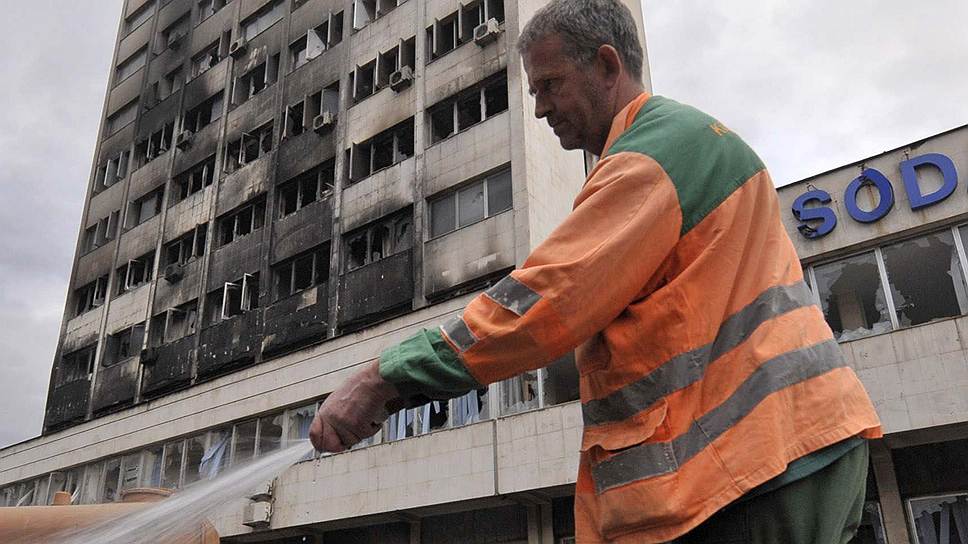 Рабочий моет улицу перед сожженным правительственным зданием в городе Тузла