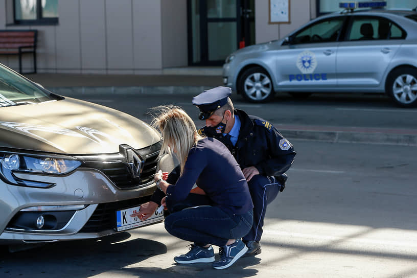 Полицейский Косово помогает заклеить государственные символы Сербии на номерном знаке