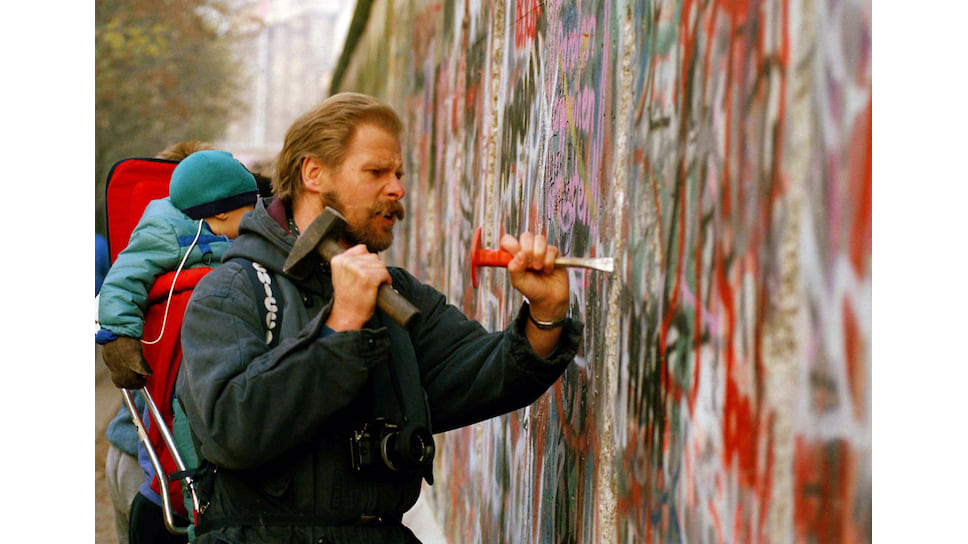 За несколько дней 1989-го стена стала историей. На фото: молодой берлинец с сыном
выбивает долотом кусочек стены на память