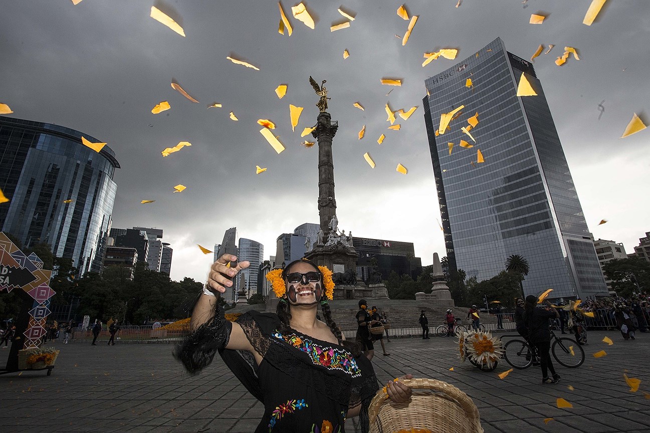 Женщина бросает бумажные цветы в воздух, на параде в День мертвых на проспекте Реформы в Мехико