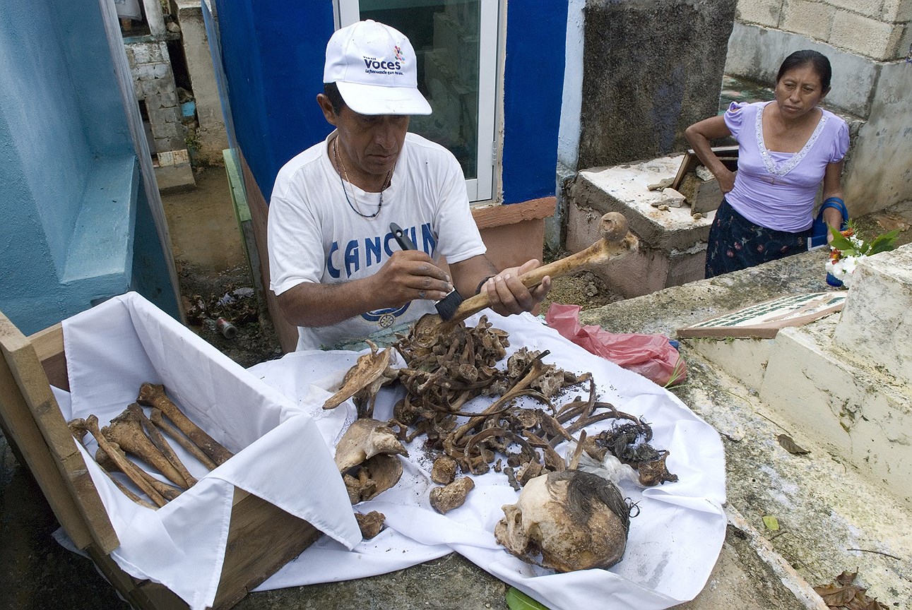 Житель поселка Помуч  очищает кости своих близких, чтобы разместить их на обозрение среди цветов и новой ткани для почитания в День мертвых