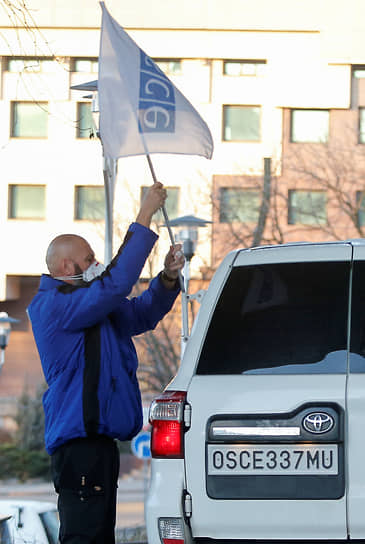 Сотрудник ОБСЕ прикрепляет флаг организации на автомобиль