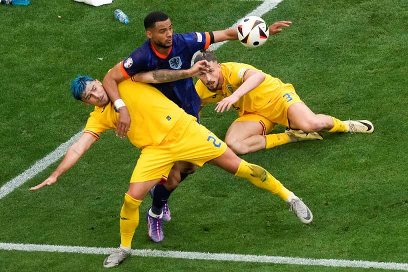 Нападающий сборной Нидерландов Коди Гакпо (в центре) пытается перехватить мяч у румынских футболистов Андрея Рациу (слева) и Раду Дрэгушина