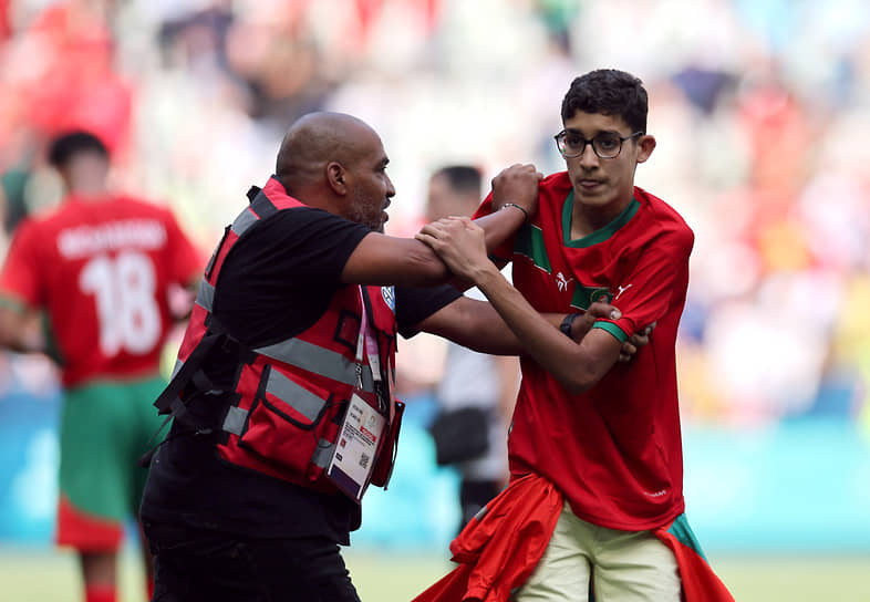 Сотрудник задерживает выбежавшего на поле болельщика после матча между сборными Аргентины и Марокко