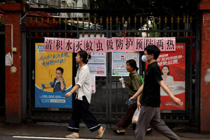 A street scene in China, possibly related to public health measures, showing people walking amidst urban infrastructure.