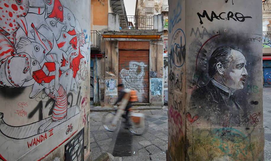 Даже когда города Италии немеют от карантина, их стены красноречивы. В этих граффити несложно увидеть намеки на мафию (справа — Марлон Брандо в роли Крестного отца). Беда в том, что ее новые боссы, как правило, изобретательнее стрит-арта