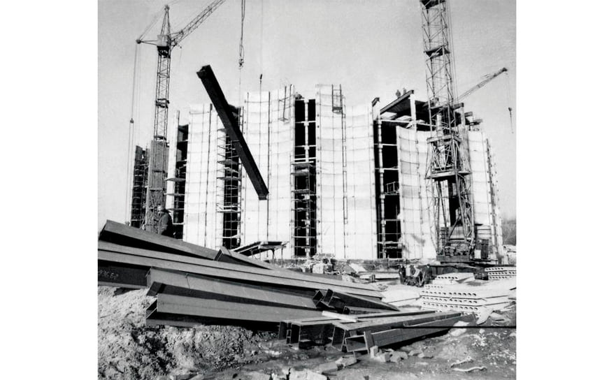 Строительство здания драмтеатра. 1976 год. Возводить объект начали в 1973 году, а закончили в 1982-м. Основные материалы — железобетон и стекло, фасад облицован белым мрамором. Здание овальной формы. Объемное решение включает 24 простенка с оконными вертикалями. Сценическая коробка сложной конфигурации поднимается над основной частью здания, общая высота которого составляет 41 метр.