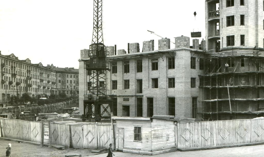 Строительство жилого дома на площади Революции, 1 в Челябинске. 1956 год. Здание планировали в стиле сталинского ампира, но в процессе строительства, завершенного в 1957 году, внесли изменения из-за борьбы с архитектурными излишествами. Изначально на первом этаже планировали открыть крупный книжный магазин, специализирующийся на литературе социалистических стран. Однако это помещение заняли различные конторы.