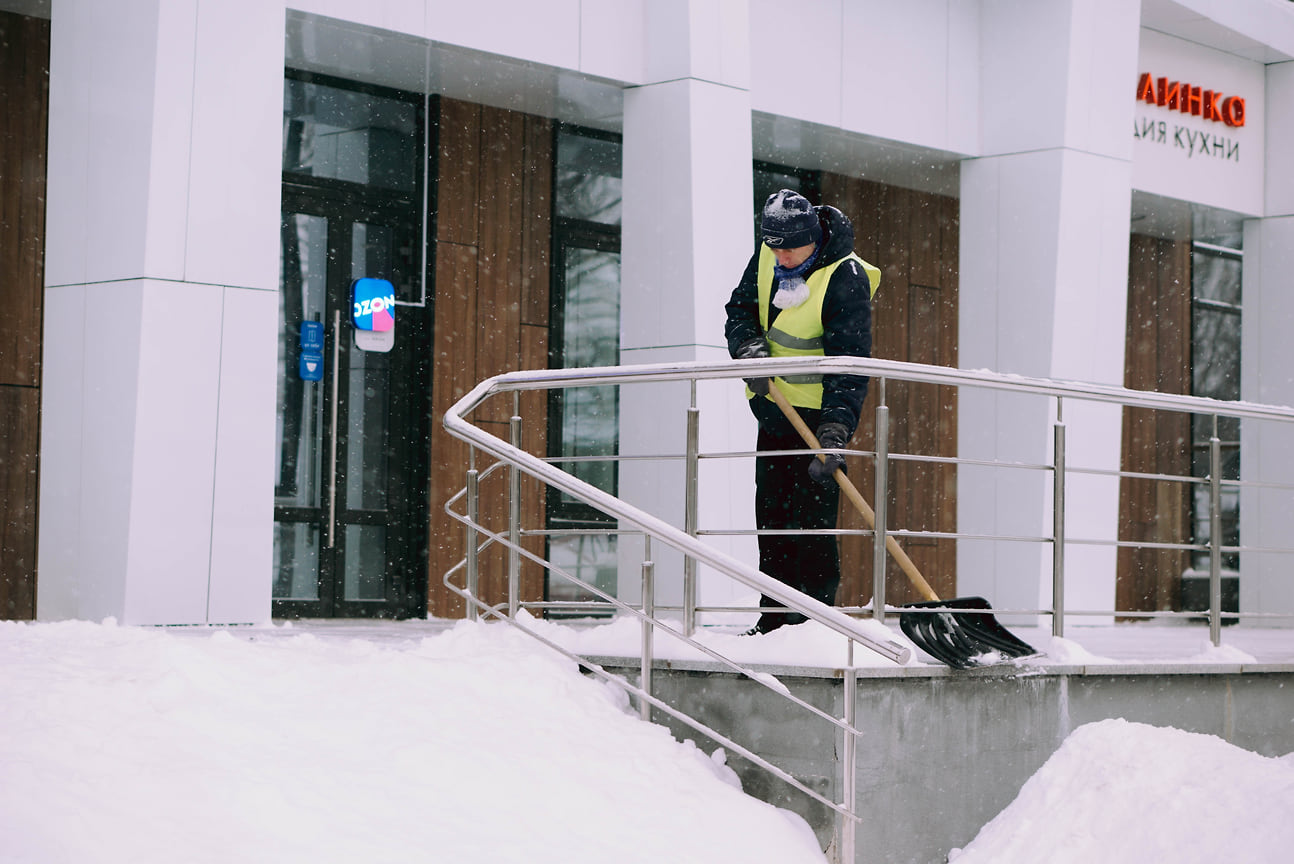 Дворник убирает снег у входа в торговый центр