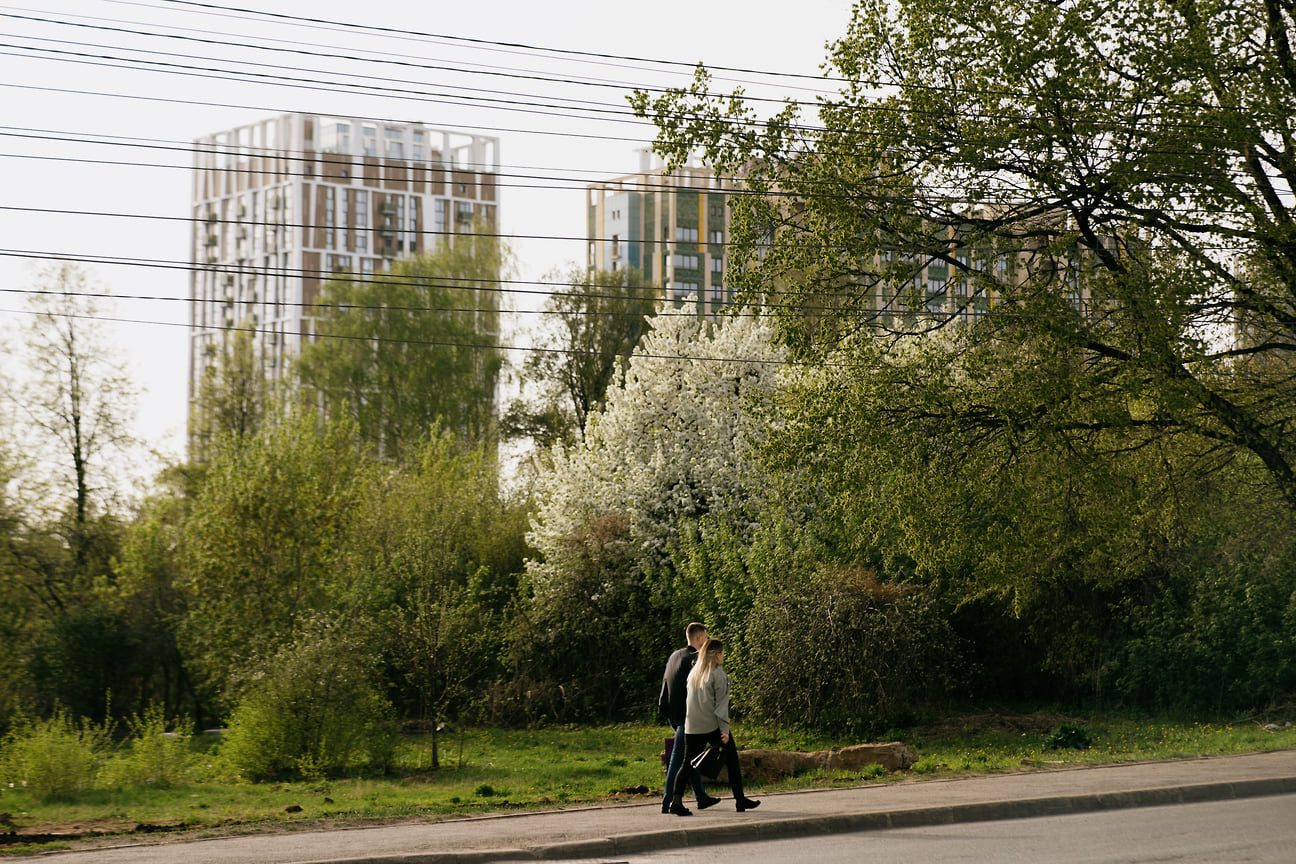 Горожане стали прогуливаться по тротуарам среди зеленых деревьев и кустарников