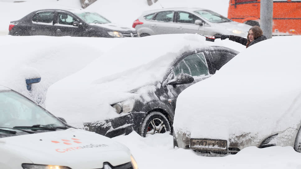 Девушка обметает автомобиль после сильного снегопада