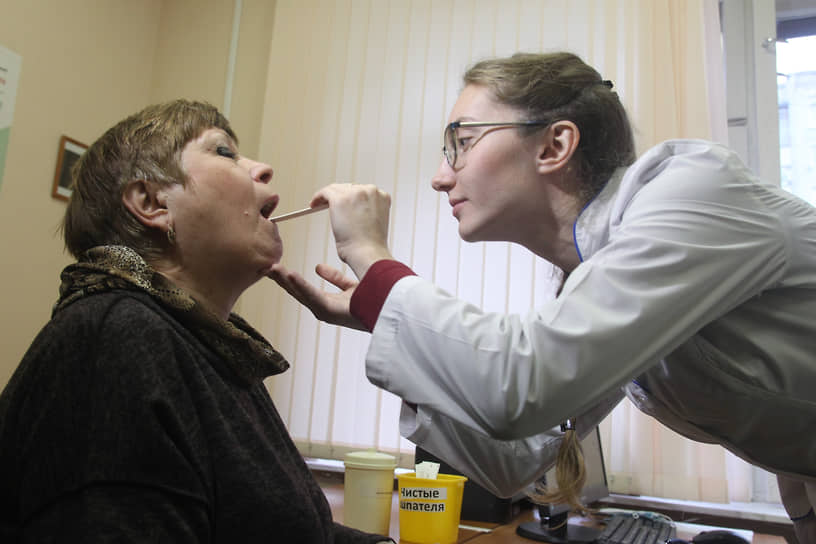Участковый врач терапевт осматривает пациентке горло