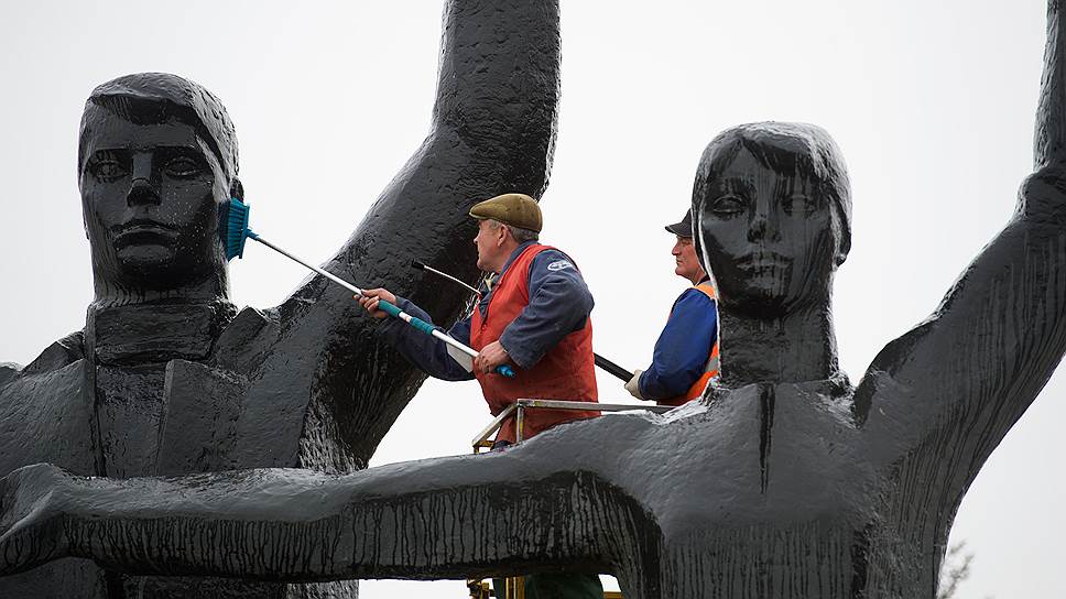 Рабочие очищают памятник в виде юноши с факелом и девушки с колосьями, которые олицетворяют преемственность поколений