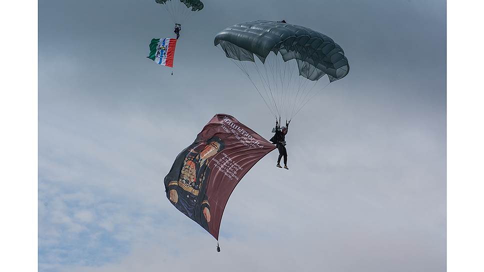 Одни из парашютистов пролетели над аэродромом с различными флагами, другие — с портретами ветеранов