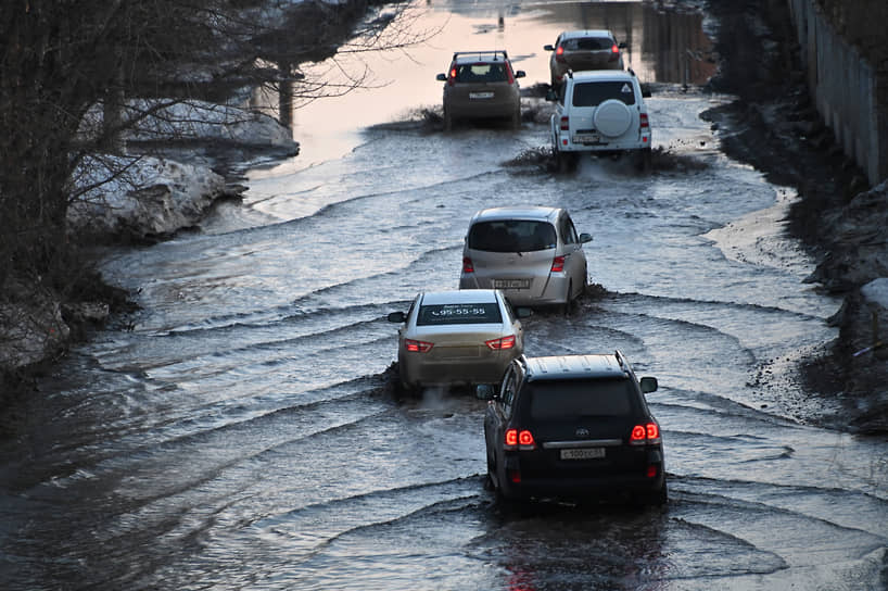 Виды Омска во время весенней распутицы.  Автомобили едут по затопленной дороге