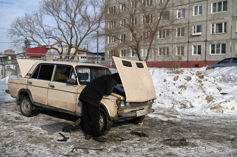 Мужчина чинит старый автомобиль во дворе жилого дома в Омске
