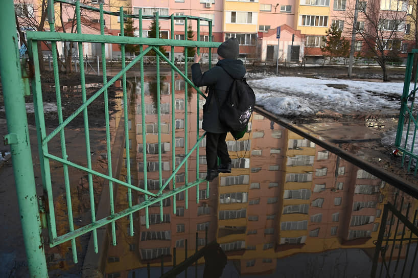 Мальчик на створке металлических ворот над лужей во дворе жилого дома во время весеннего паводка в Омске